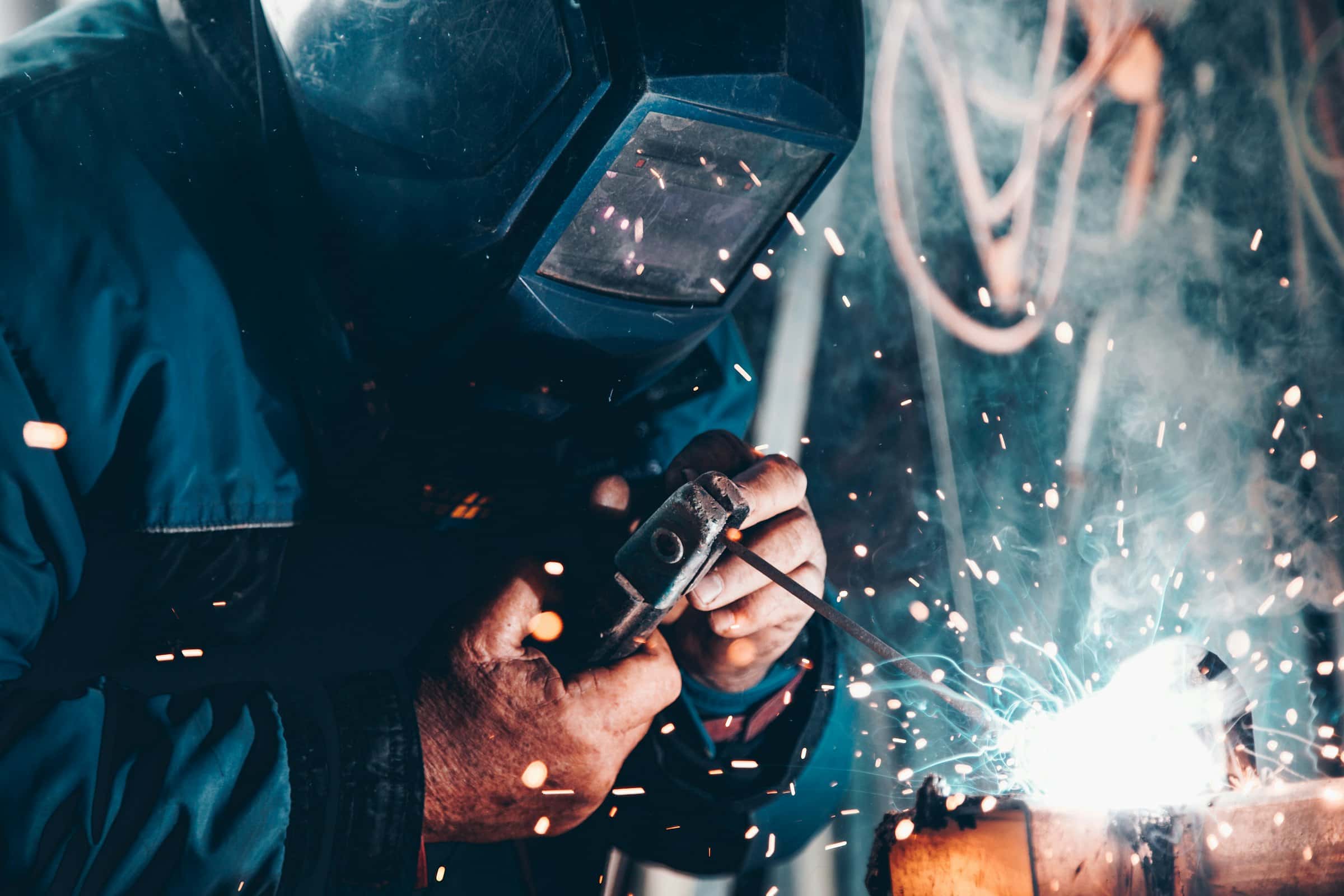 A welder working carefully in a dark workshop, sparks lighting the bench